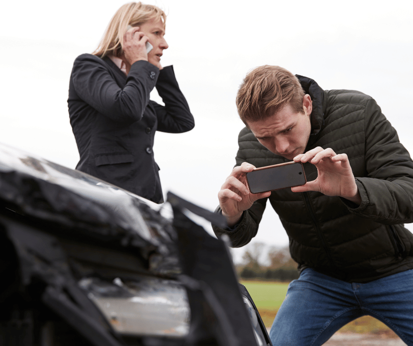 Person documenting a crash scene beside damaged vehicles.